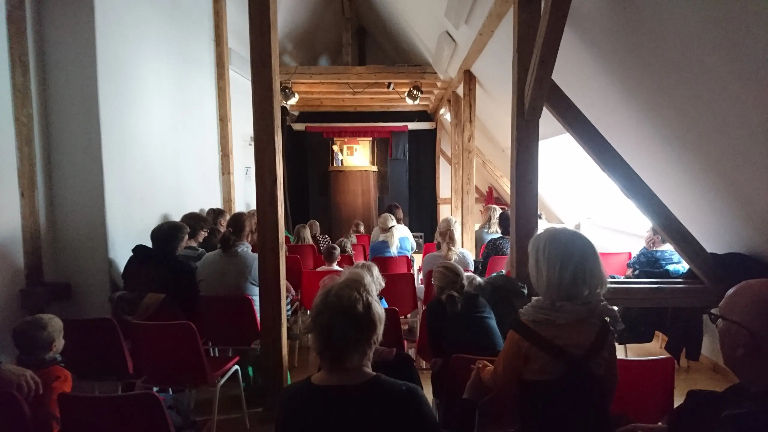 Zuschauer in Stuhlreihen vor einem Puppentheater.