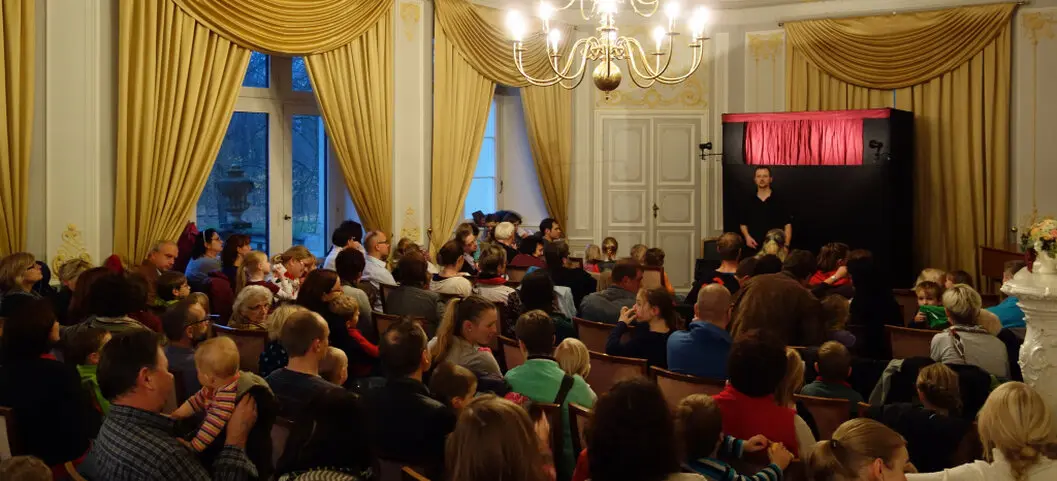 Familien vor eine Puppenbühne in einem Barocksaal